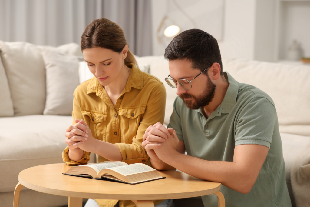Christian married couple praying together over an open Bible at home